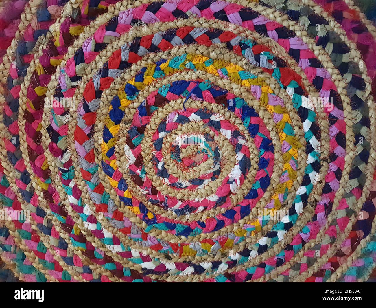 Close-up of fabric interwoven with natural fiber, colored in spiral shape, creative placemat, full screen, top view. Stock Photo