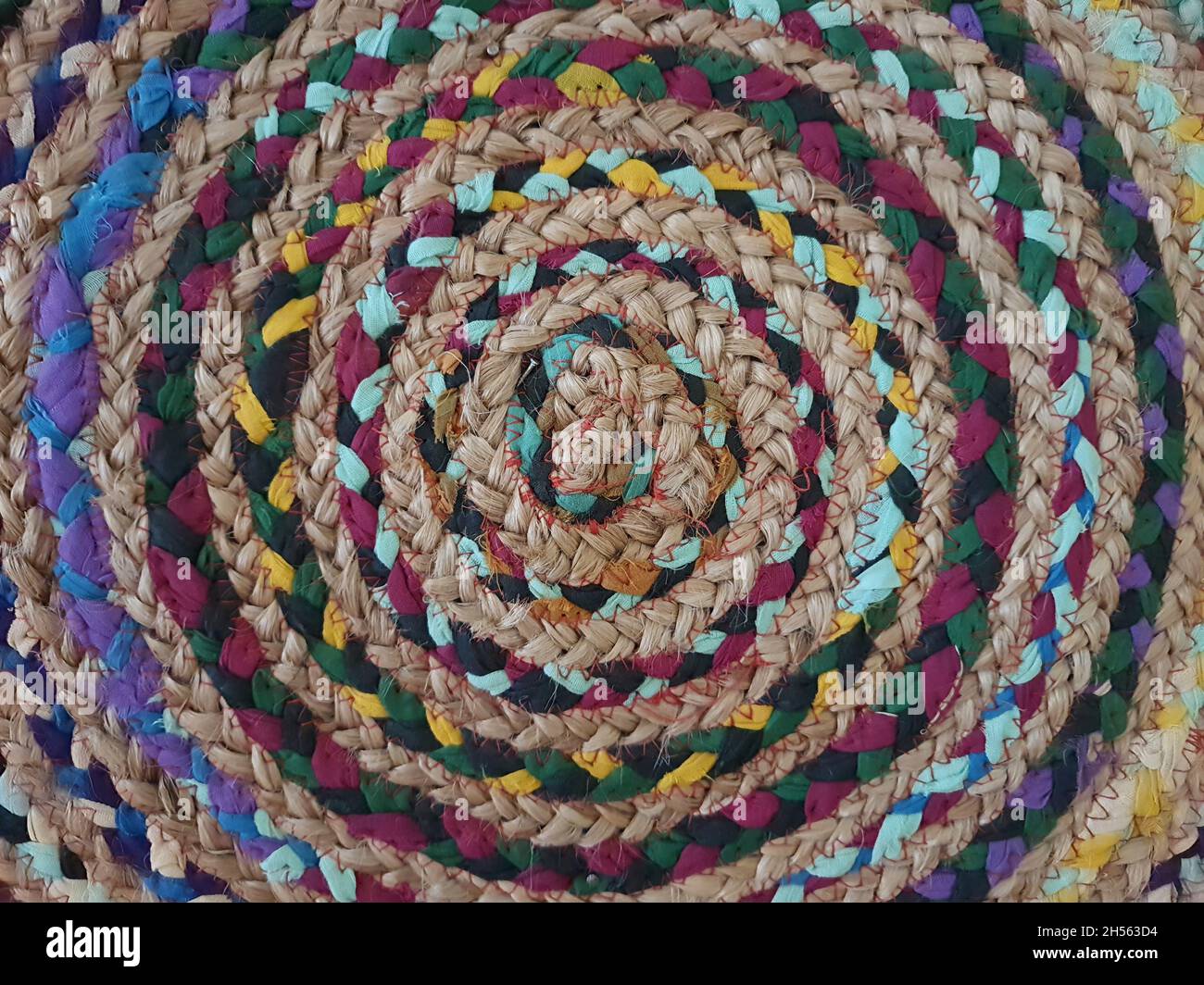 Close-up of fabric interwoven with natural fiber, colored in spiral shape, creative placemat, full screen, top view. Stock Photo