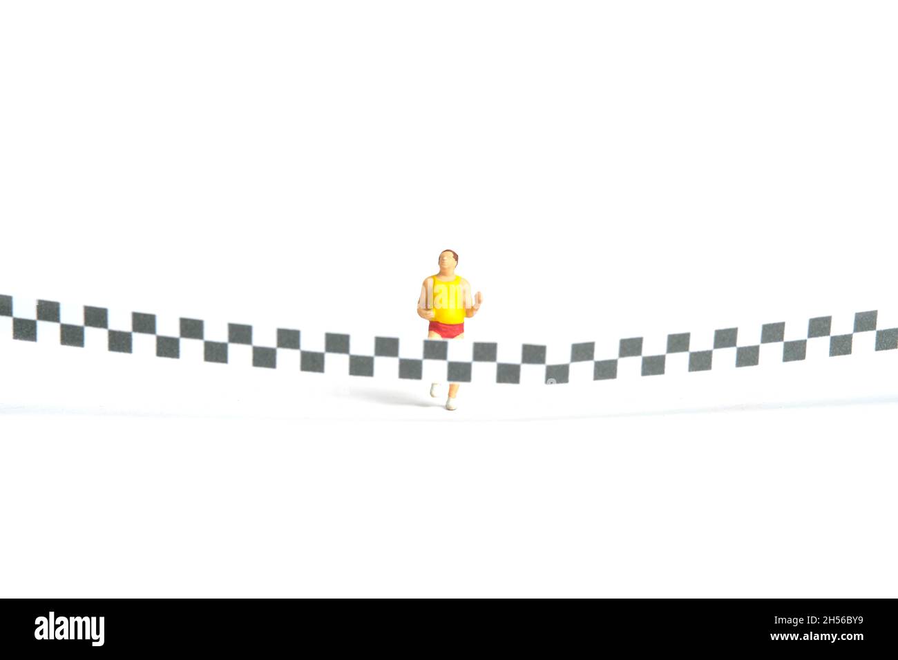 Miniature people toy figure photography. A fat man running towards the finish line, isolated on white background. Image photo Stock Photo