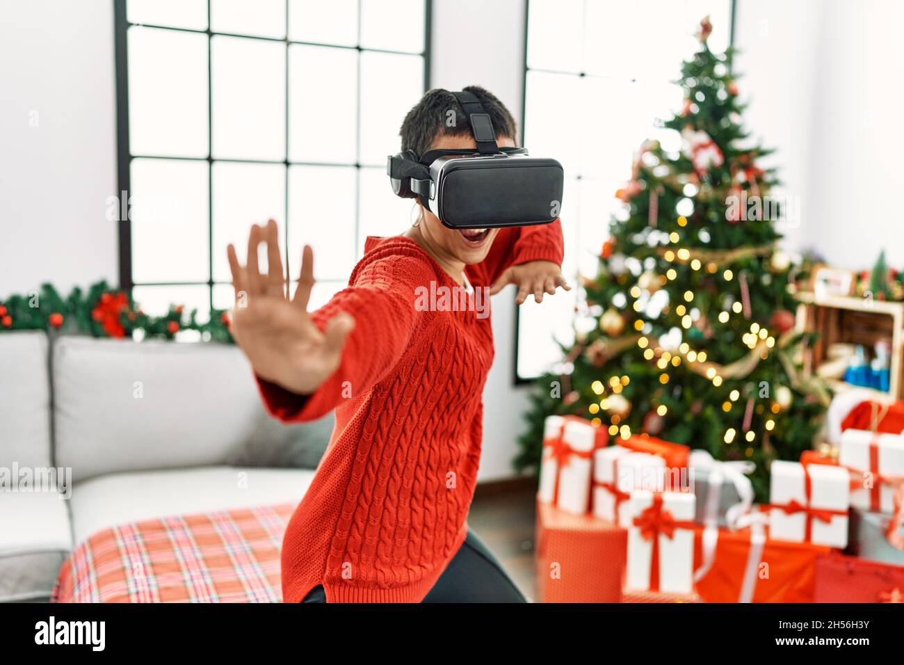 Young hispanic woman playing video game using vr glasses standing by ...