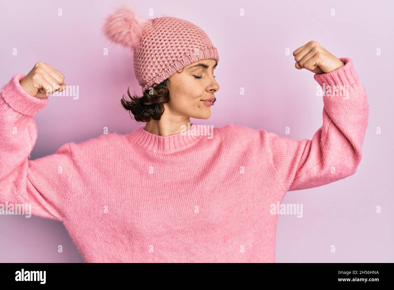 Young brunette woman wearing cute wool cap showing arms muscles smiling proud. fitness concept. Stock Photo