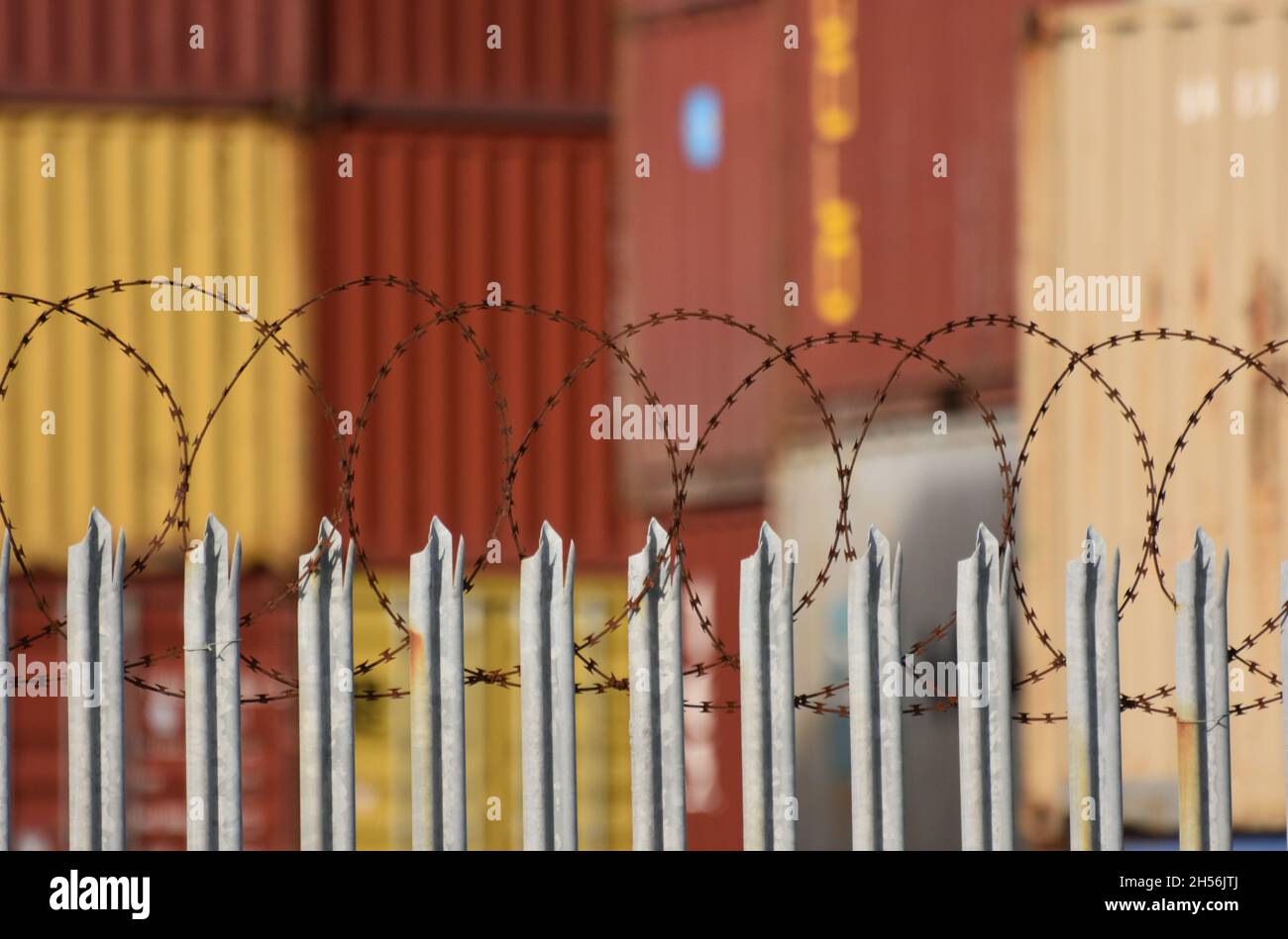A razor barbed wire topped fence in front of freight shipping containers piled up at one of the UK’s busiest shipping terminals Stock Photo