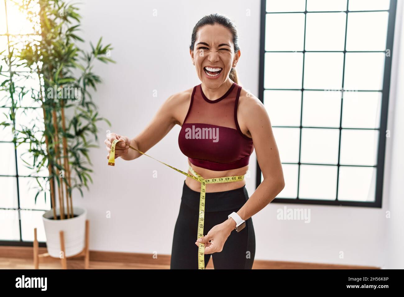 Young hispanic woman wearing sportswear using tape measure at sport