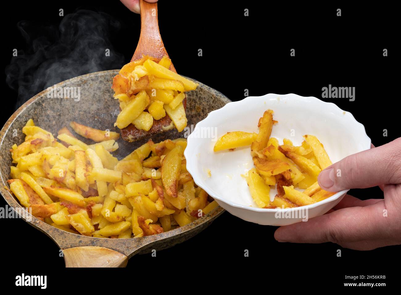 Hand of the chef putting delicious crispy golden hot fried potato wedges into a white plate with a wooden spatula close-up. Delicious homemade food. A Stock Photo