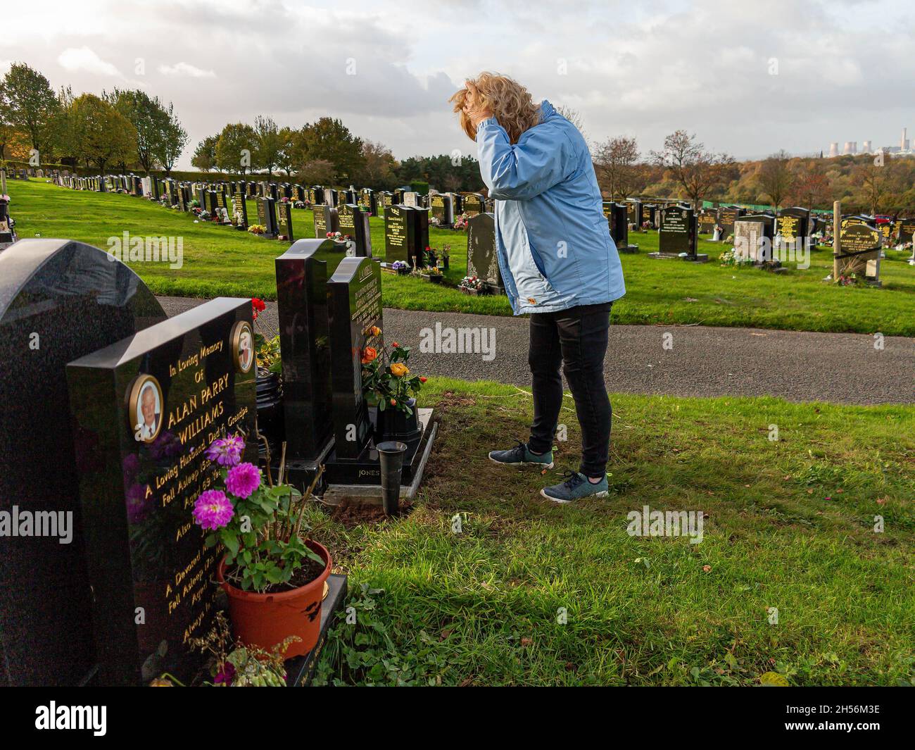 Upset lady puts hands on head whilst standing at parent's grave Stock Photo