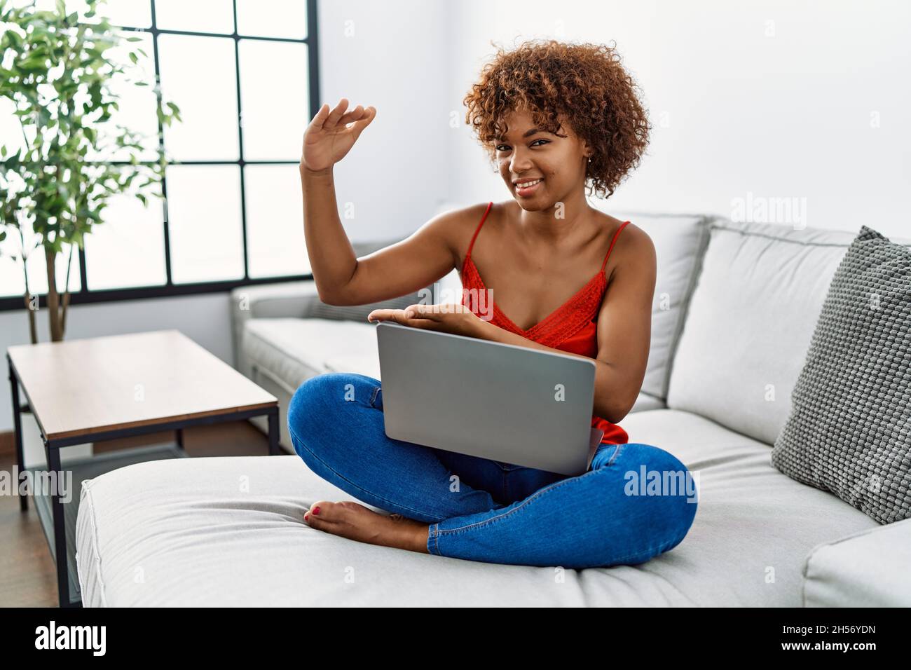 Young african american woman sitting on the sofa at home using laptop ...