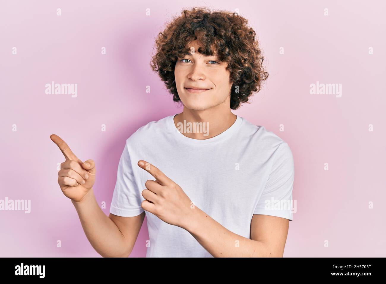 Handsome young man wearing casual white t shirt smiling and looking at ...