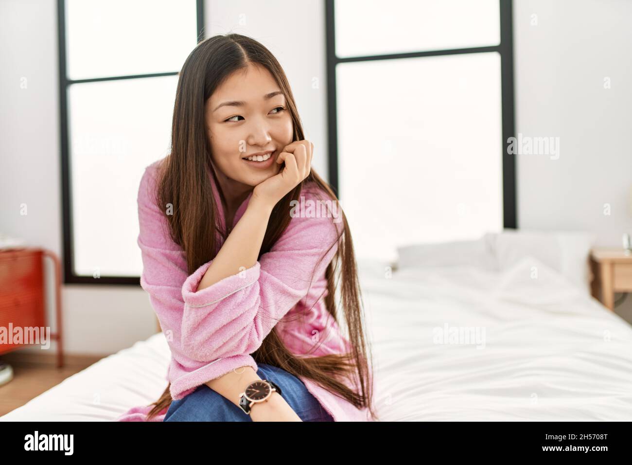 Young chinese girl smiling happy sitting on the bed at bedroom Stock ...