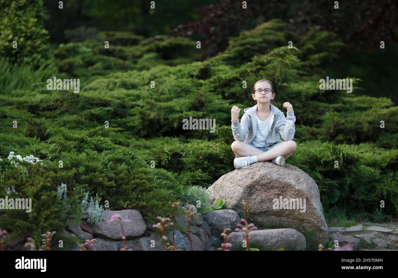 Child girl sitting on the cobblestone in lotus position. Teenage girl practicing yoga. Stock Photo