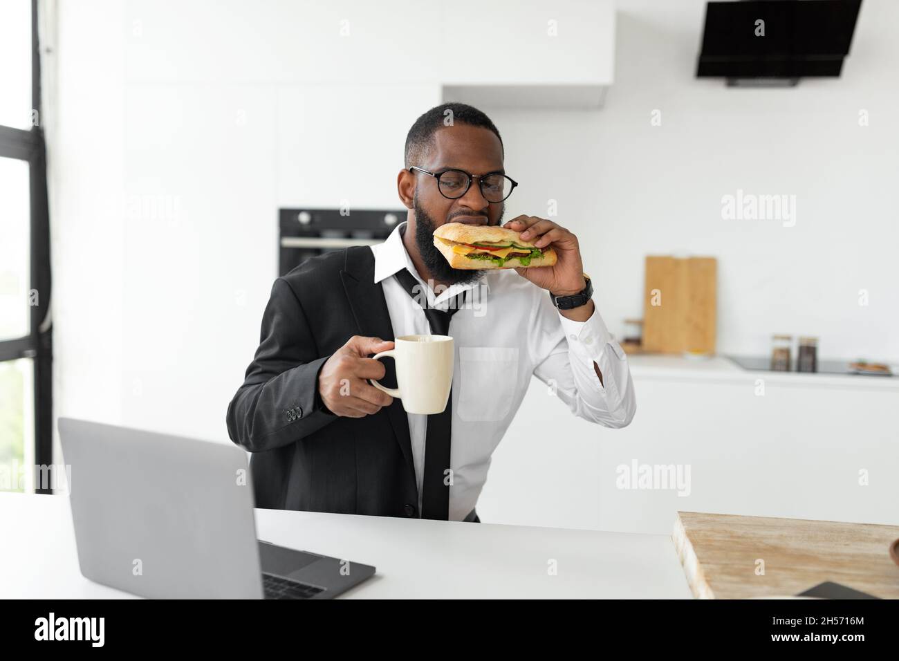 Black man rushing to work eating sandwich at home Stock Photo