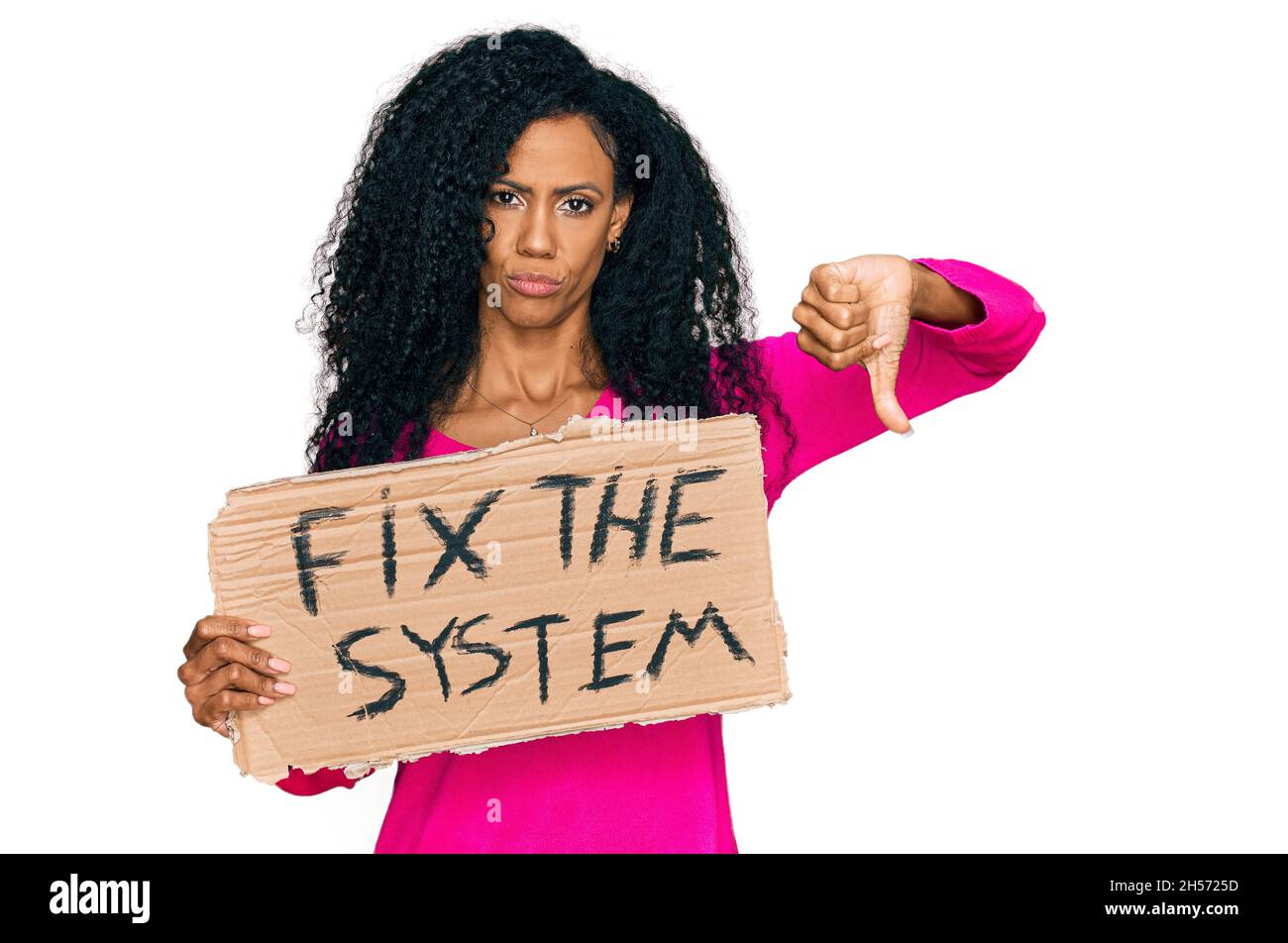 Middle age african american woman holding fix the system banner cardboard with angry face, negative sign showing dislike with thumbs down, rejection c Stock Photo