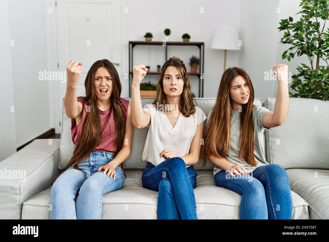 Group of three hispanic girls sitting on the sofa at home angry and mad ...