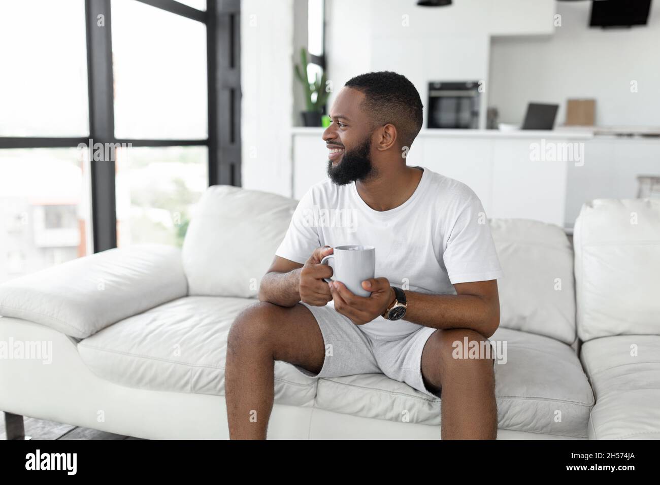 Smiling African American man drinking coffee sitting on couch Stock Photo
