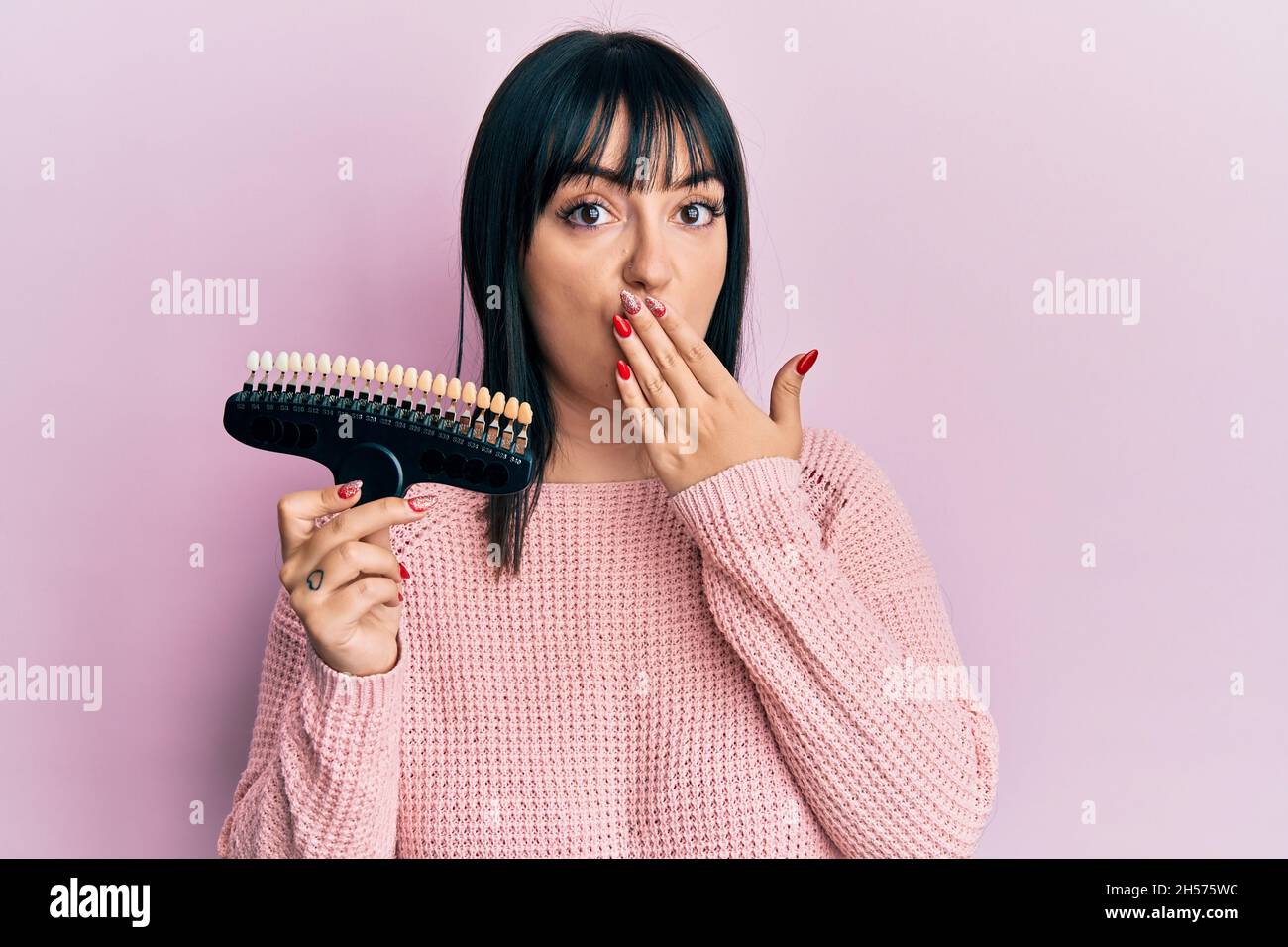 Young hispanic woman comparing teeth whitening covering mouth with hand, shocked and afraid for mistake. surprised expression Stock Photo