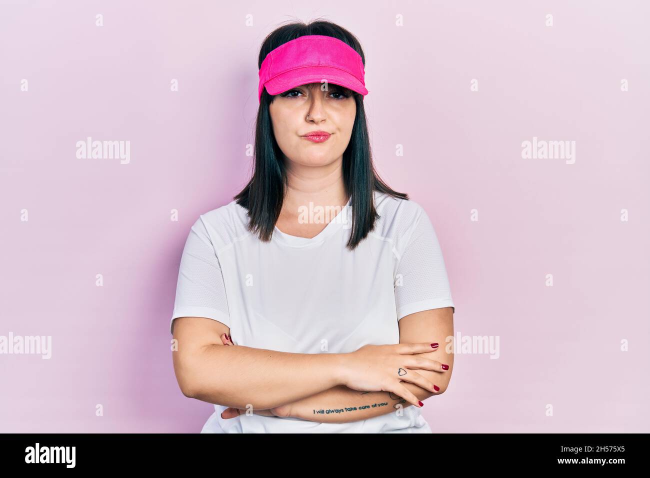 Young hispanic woman wearing sportswear and sun visor cap skeptic and nervous, disapproving expression on face with crossed arms. negative person. Stock Photo