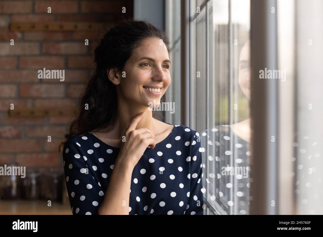 Happy young hispanic female looking through big window dreaming indoors Stock Photo