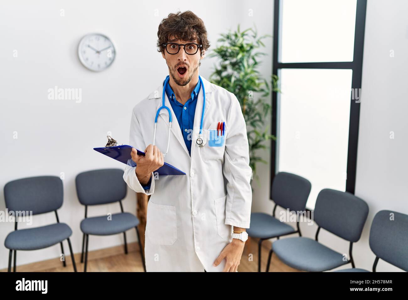 Young hispanic doctor man at waiting room in shock face, looking ...
