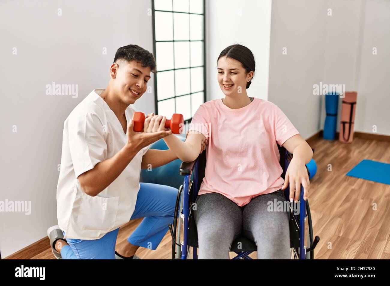 Young disabled woman sitting on wheelchair making mobility exercise using dumbbells at the