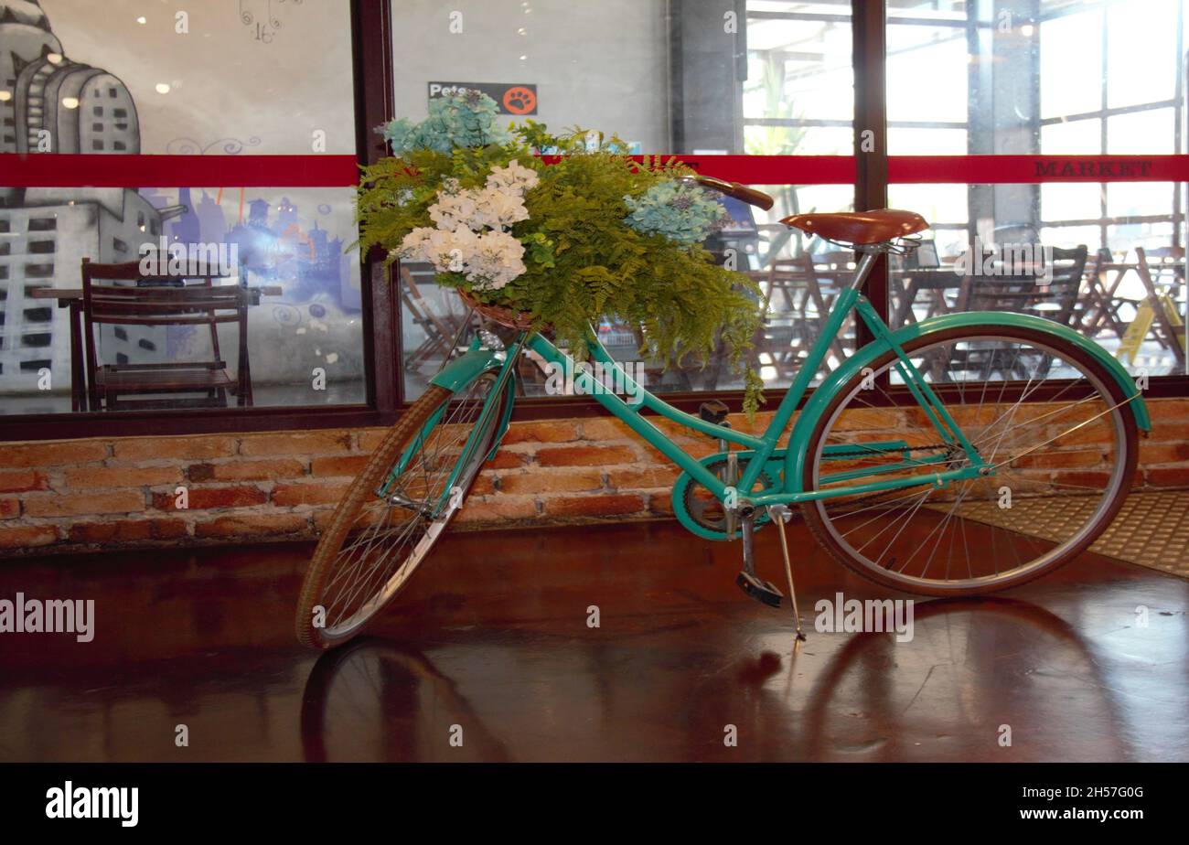 Refurbished old bicycle, painted green with a basket with flowers, on display in a store. Stock Photo