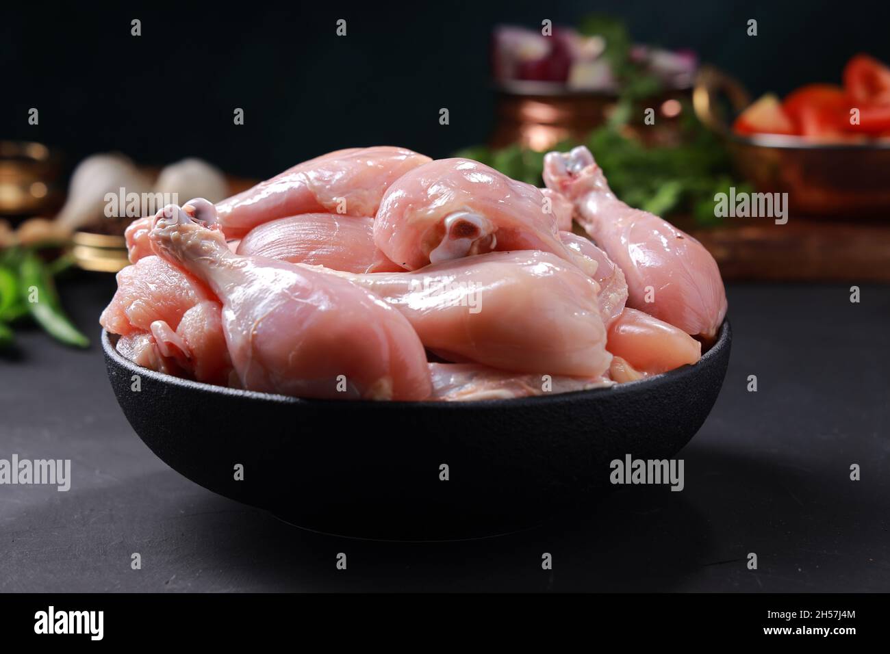 Raw chicken biriyani cut without skin arranged on black container with cooking ingrediants placed nearby. Stock Photo