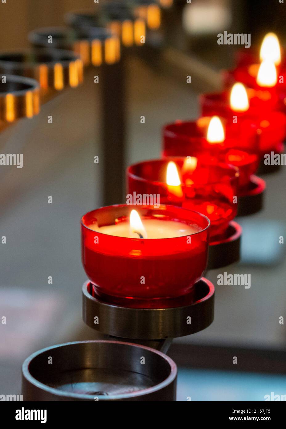 Burning red prayer candles inside a catholic church on a candle rack