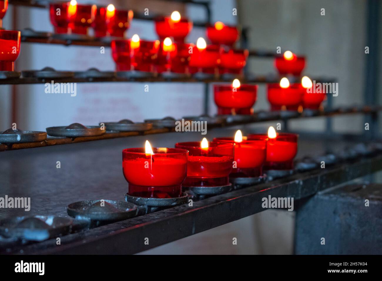 Burning red prayer candles inside a catholic church on a candle rack. Selective focus Stock