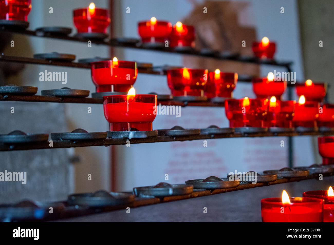 Burning red prayer candles inside a catholic church on a candle rack
