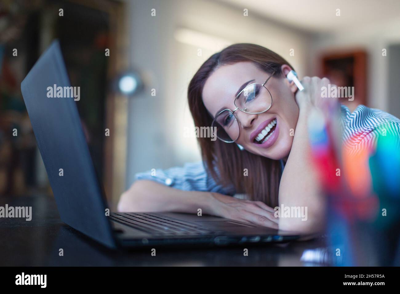 Happy young positive Caucasian woman with hands free device toothy smile at laptop Stock Photo