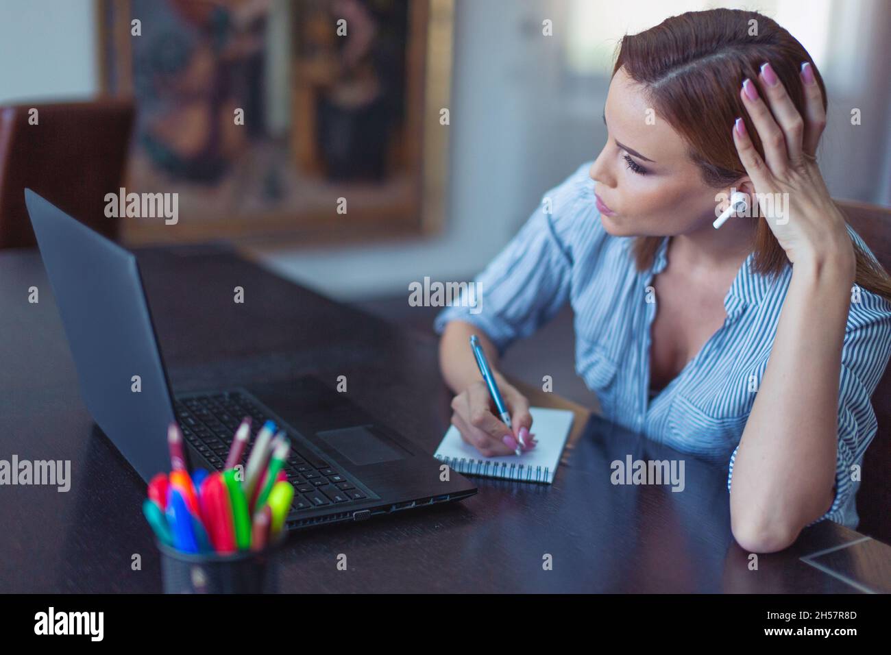 Young businesswoman making notes while communicating online at home office Stock Photo