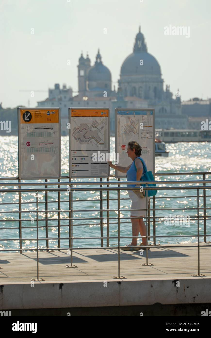 A tourist looks at tables and maps of ferries in Venice Italy. In the background the church of Saint George Stock Photo