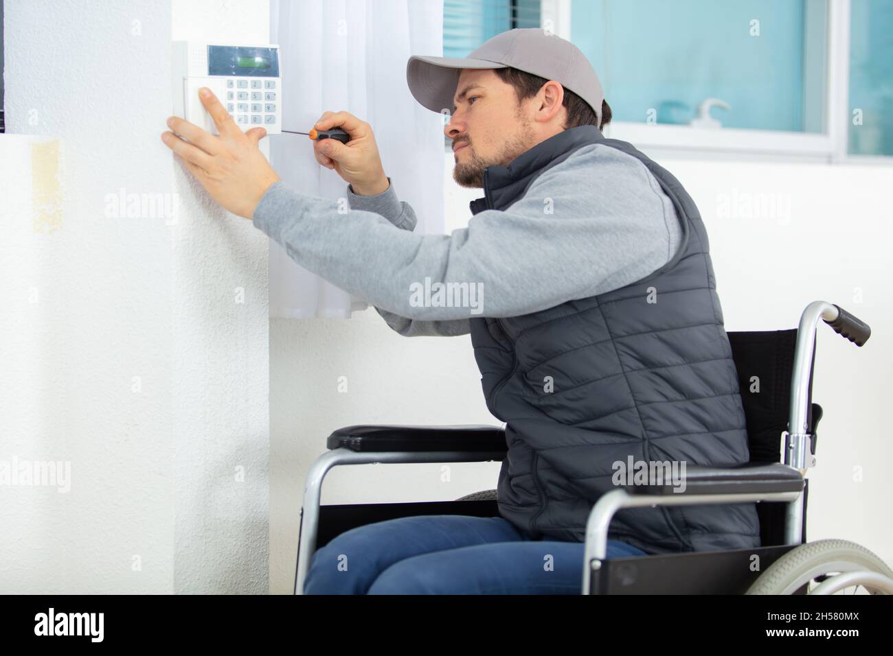 invalid young electrician installing security alarm on wall Stock Photo