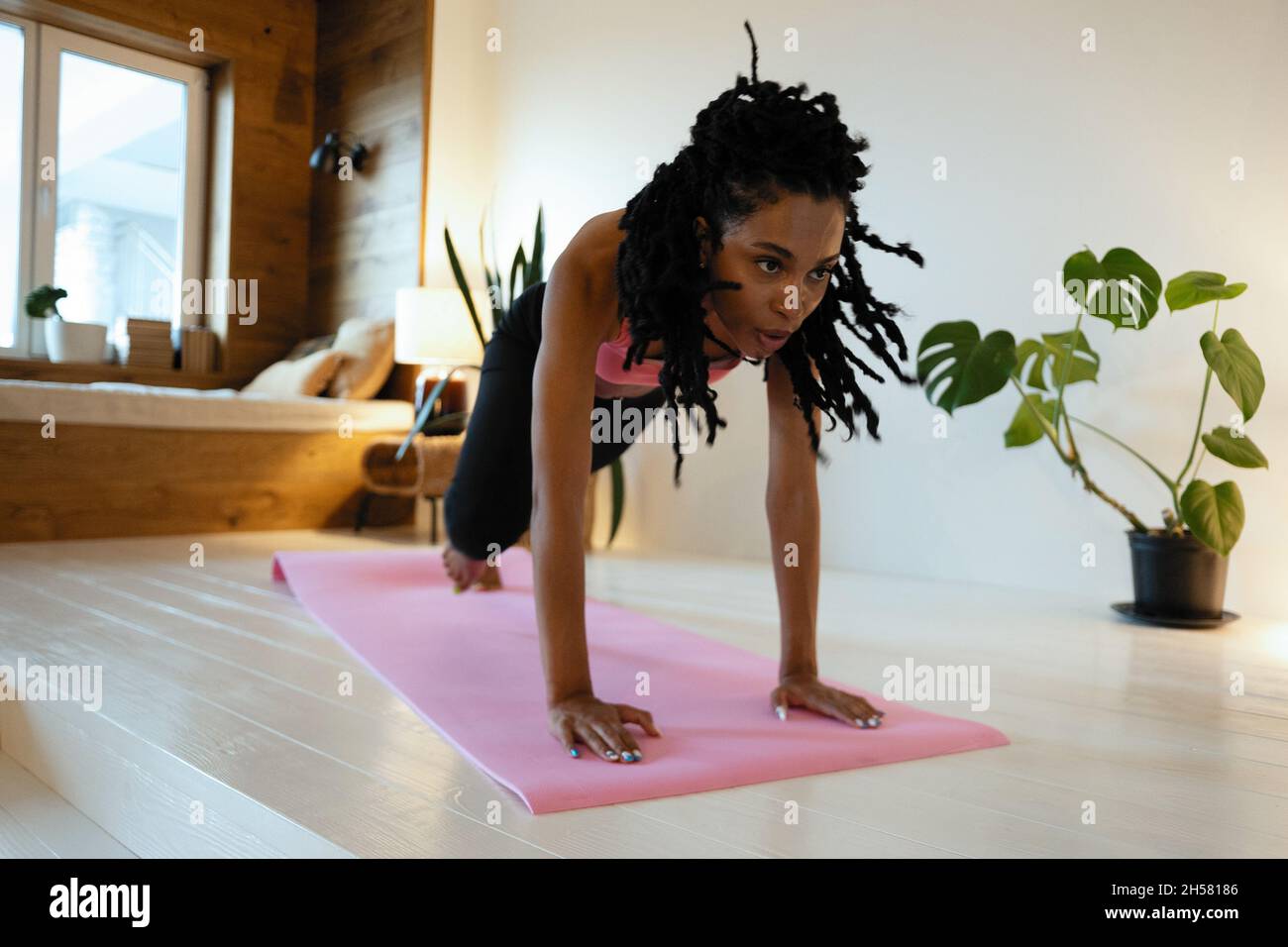 Strong Beautiful Fitness Girl in Athletic Workout Clothes is Doing a Plank Exercise. She is Training at Home in Her Living Room with Cozy Interior. Stock Photo