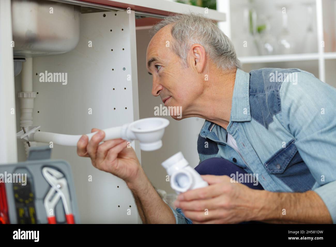 senior citizen using pipe wrench to tightenup pipes under sink Stock