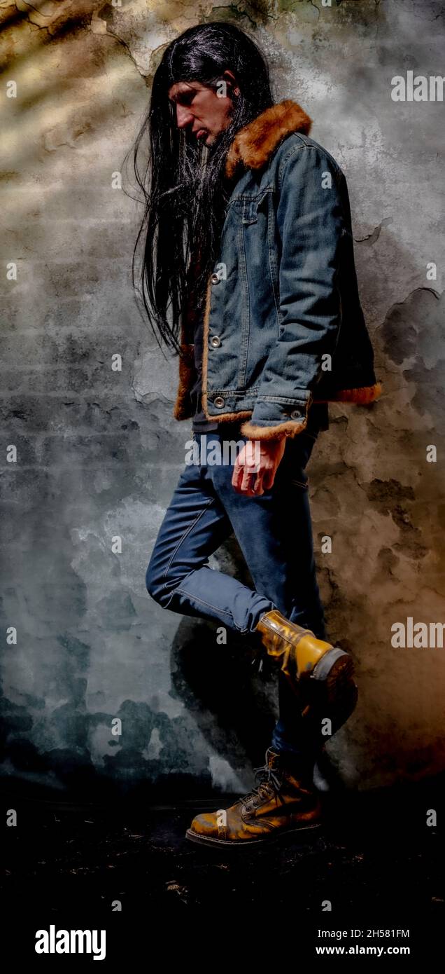 Black long hair man with jeans and big yellow shoes and old wall Stock Photo
