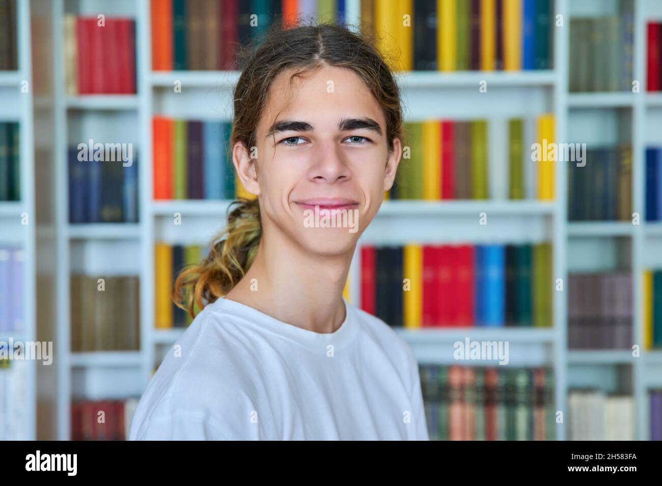 Portrait of a smiling teenage boy looking at the camera in the library. Stock Photo