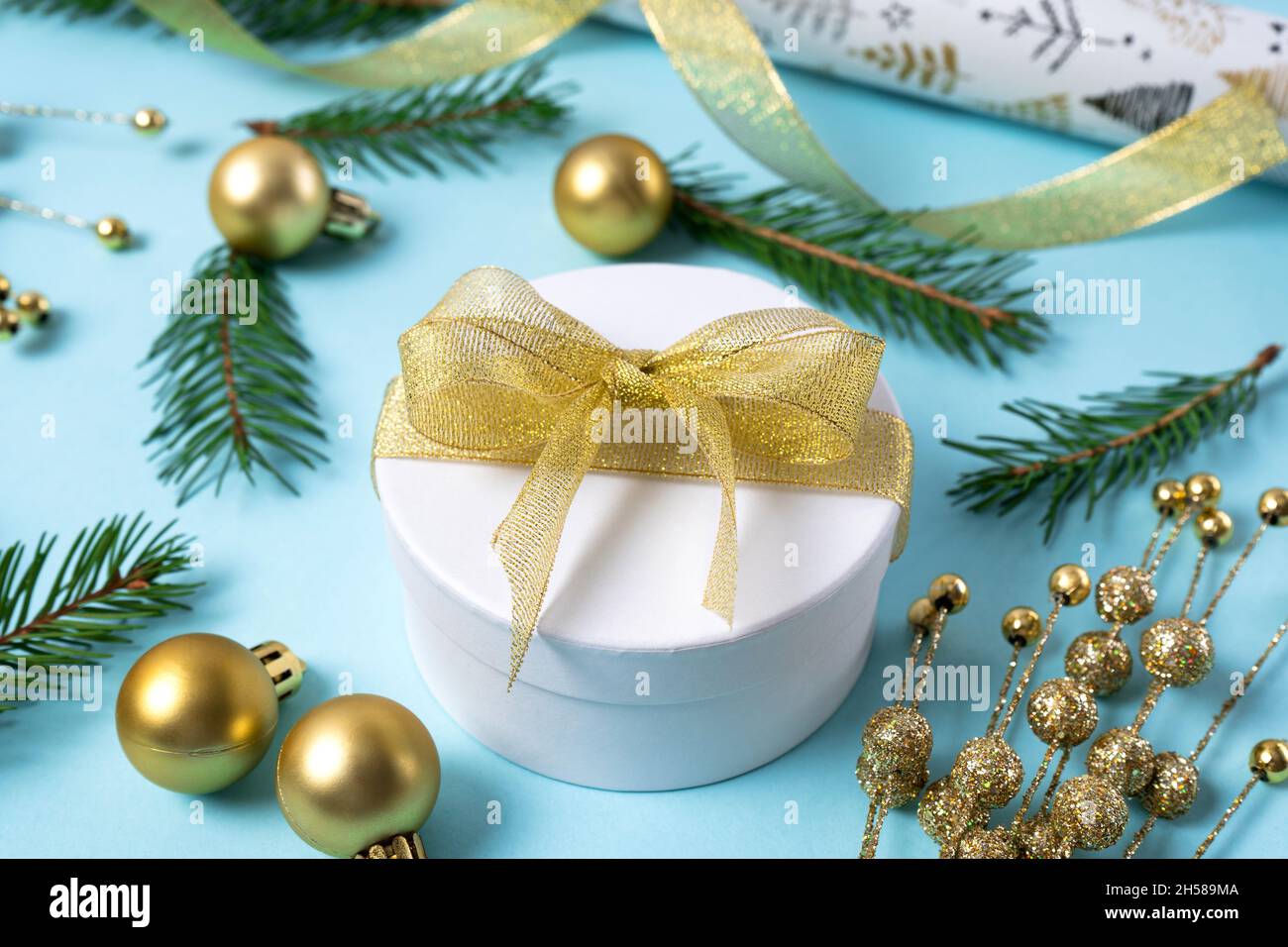 Gift box with gold ribbon. Christmas gold decorations on a light blue background. Holiday and celebration concept for postcard or invitation. Side vie Stock Photo