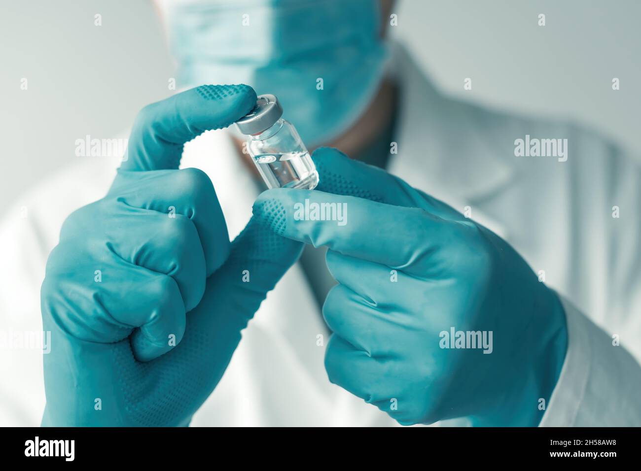Medical professional with protective gloves and face mask holding booster shot Covid-19 vaccine bottle vial in hospital, selective focus Stock Photo