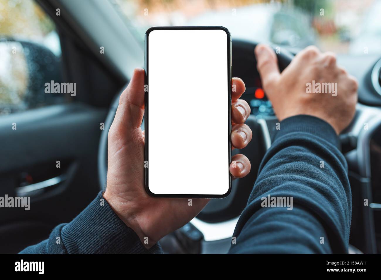 Car driver holding mobile smart phone over steering wheel, blank whgite screen as copy space, selective focus Stock Photo