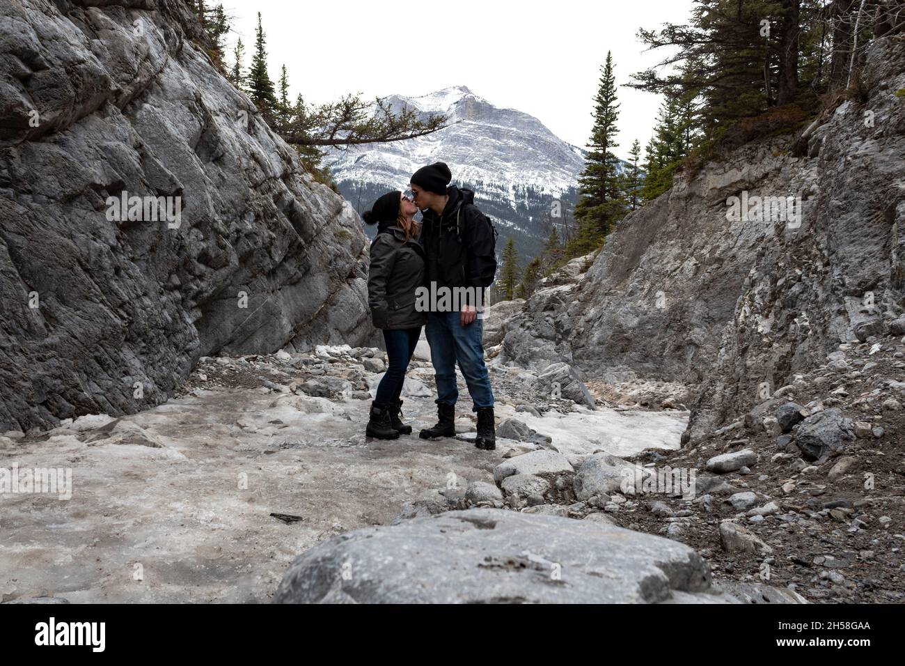 Couple standing on Grotto Mountain kissing. mountains in background. overcast sky. rocks, trees. Stock Photo
