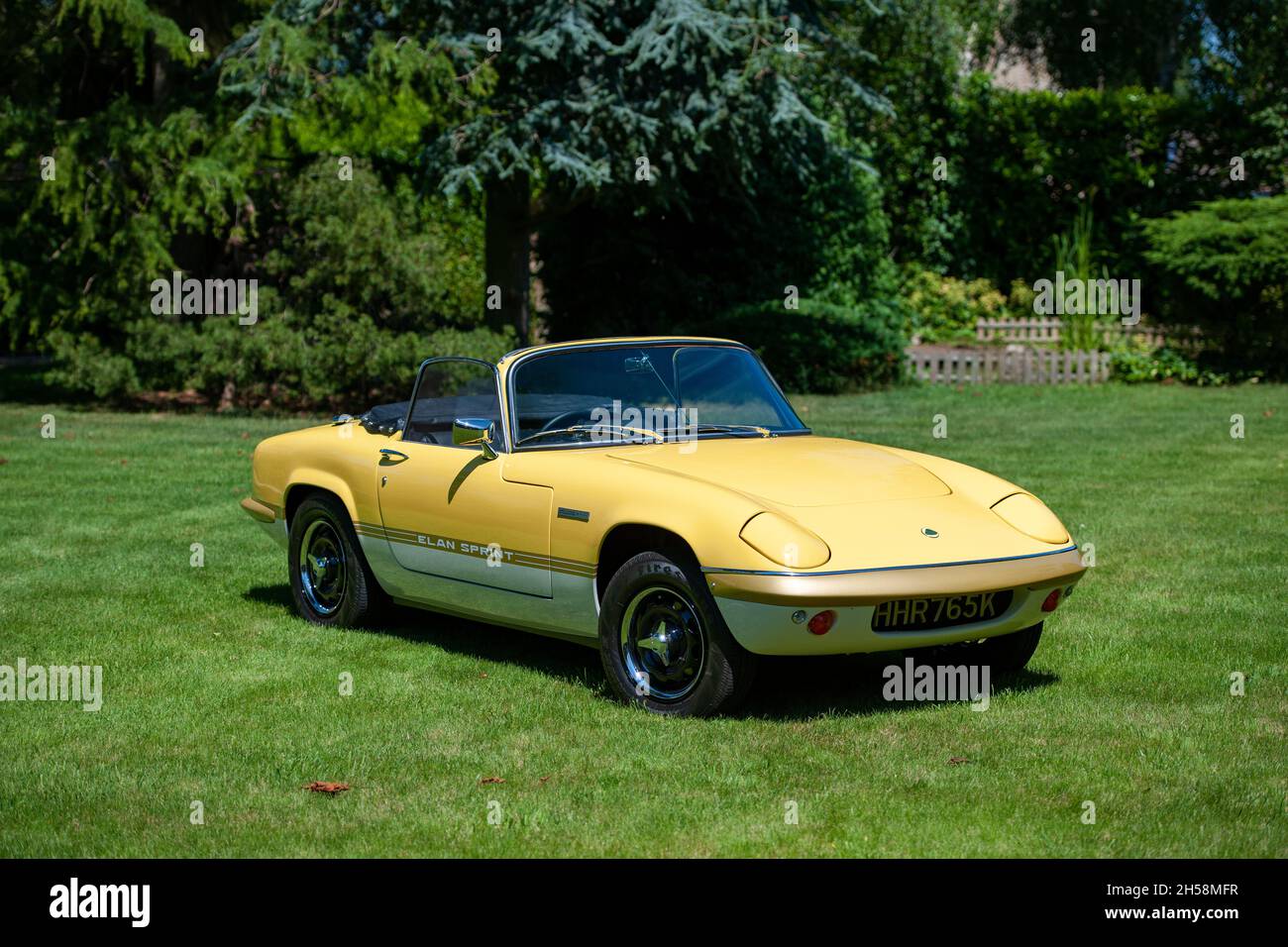 Yellow Lotus Elan Sprint convertible parked on a lawn with trees and garden behind on a sunny Summer day Stock Photo