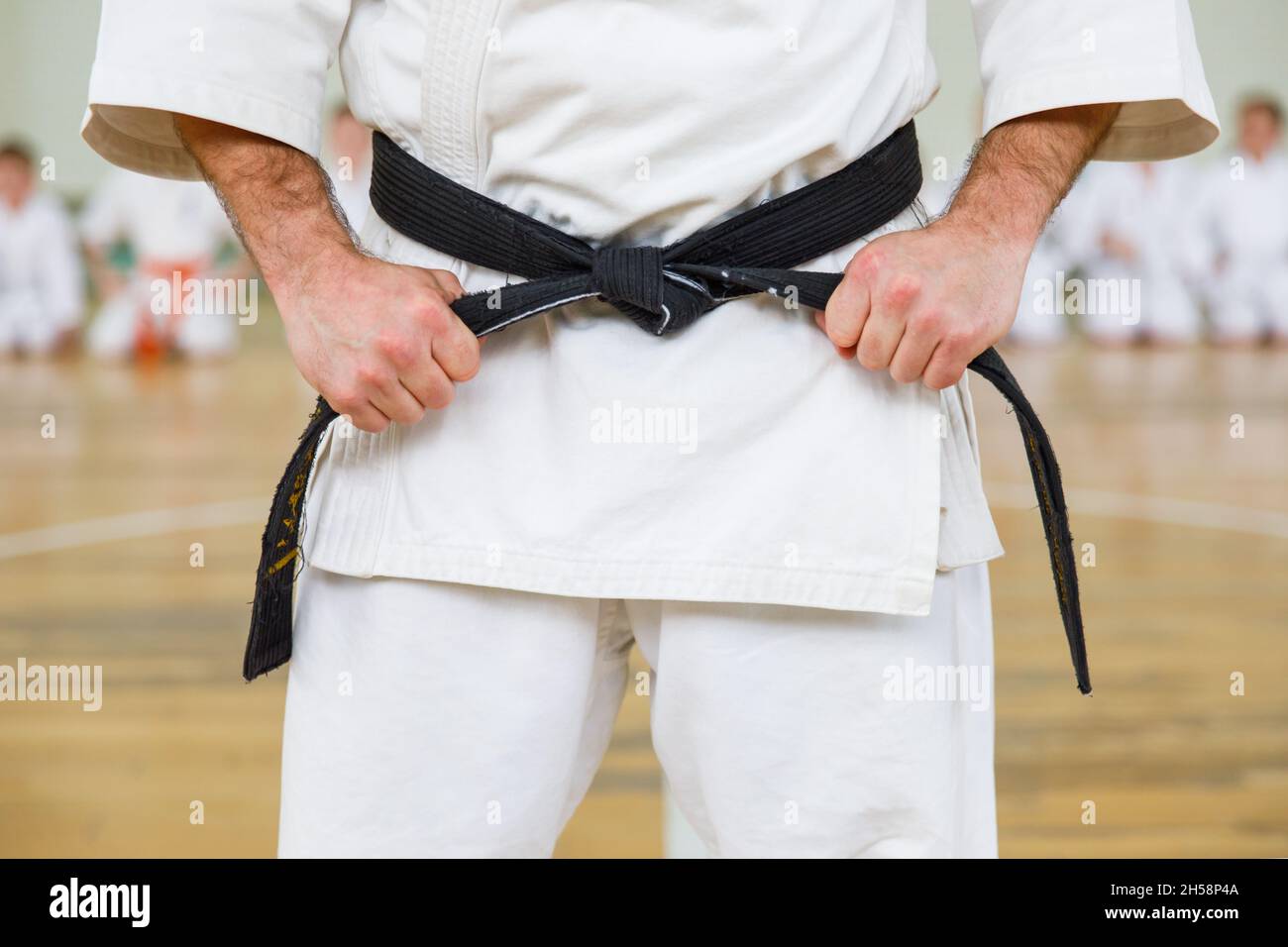 Karate master in a white kimono and with a black belt, stands in front of the formation of his students. Martial arts school in training in the gym Stock Photo