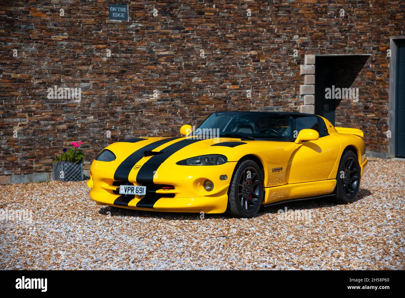 Yellow Dodge Viper SRT 10 parked on a gravel forcourt in front of a house and garage Stock Photo