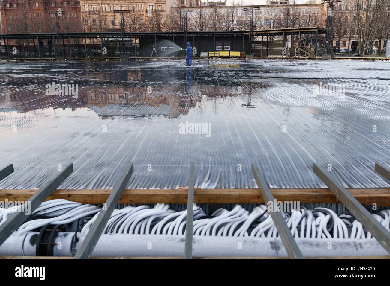 Filling ice rink with water workman holding hose pouring water on refrigeration piping system