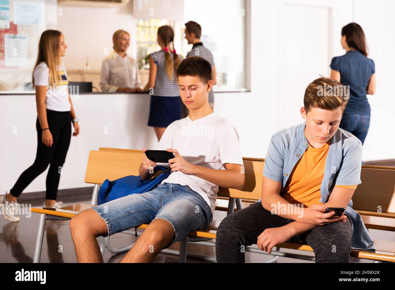 Teenagers using smartphones in college hall Stock Photo