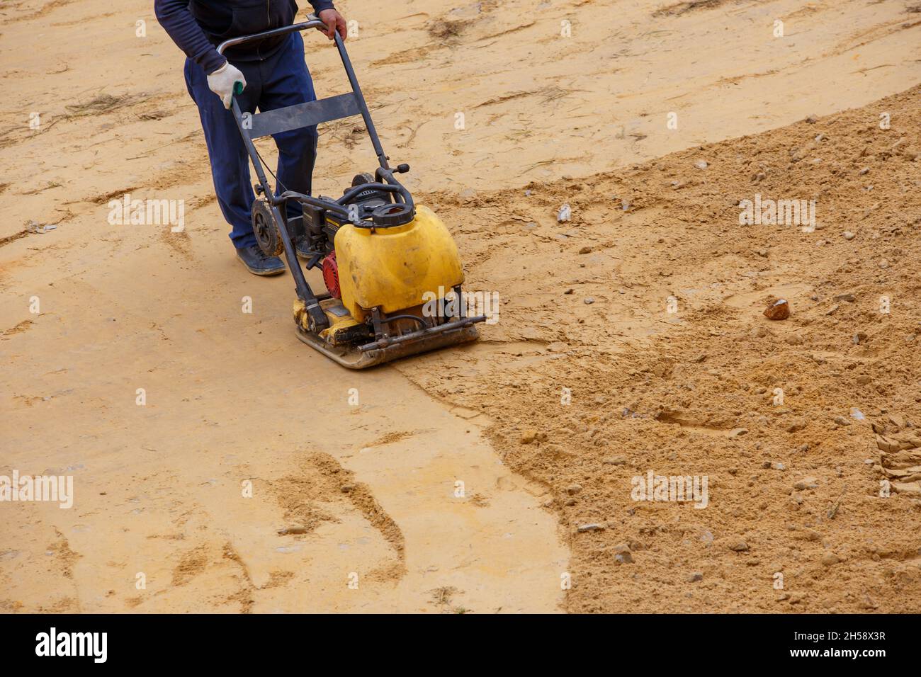 Worker in use vibratory plate compactor for compaction sand during
