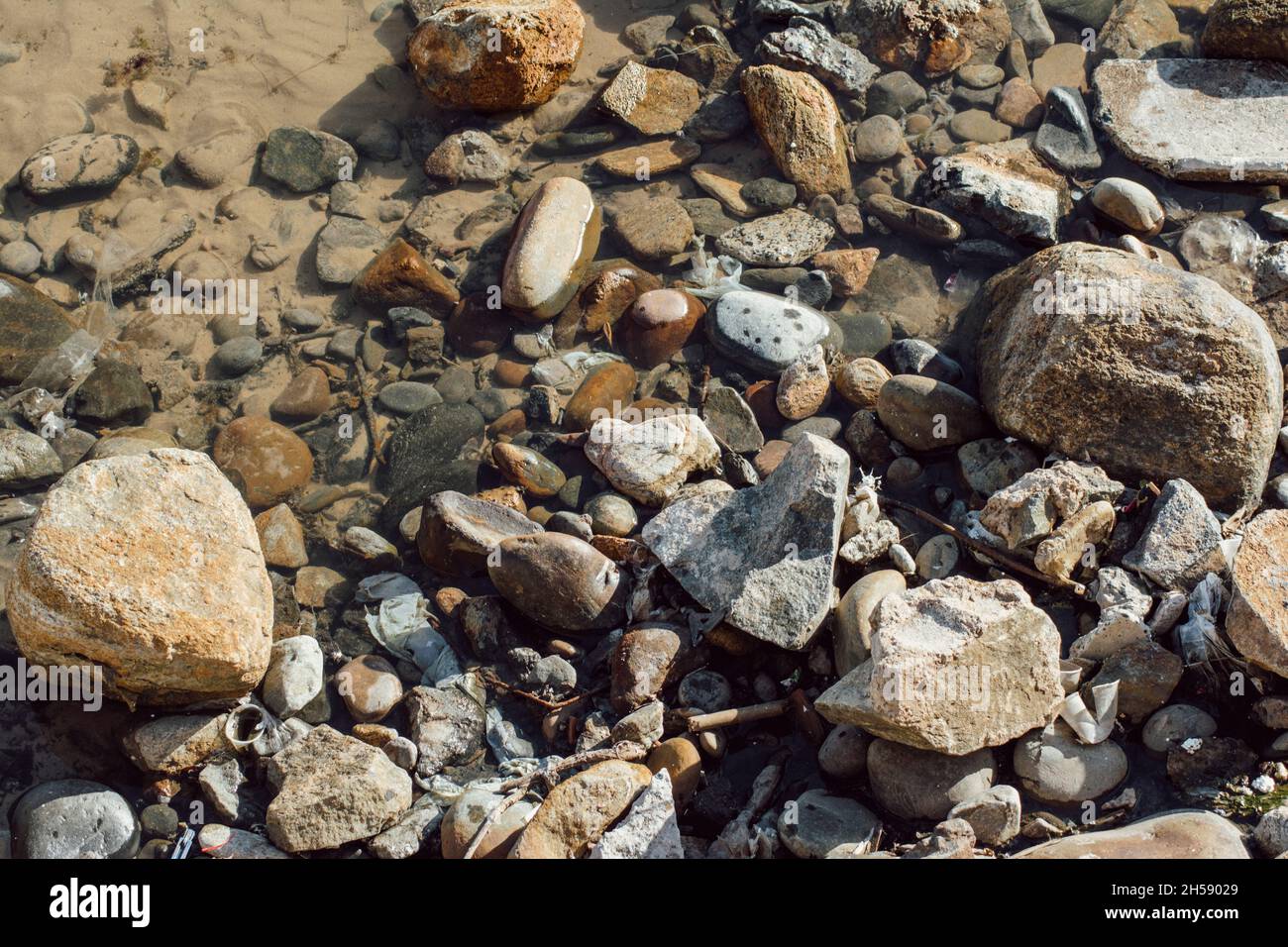 Stones and rocks in brown, gray and black on the shore of Ondina beach ...