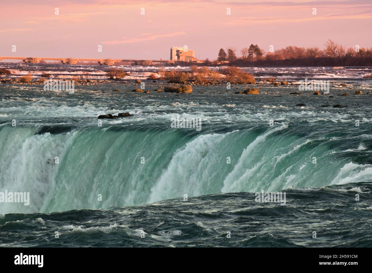 Green waters of Niagara river dashing downd from the edge of Horseshoe Falls in front of spectacular sunset sky. Horseshoe Falls, also known as Canadi Stock Photo