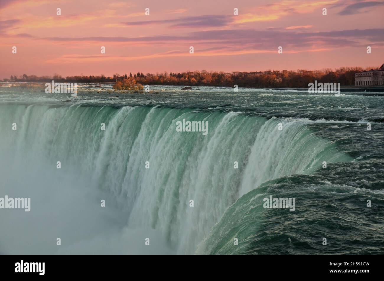 Green waters of Niagara river dashing downd from the edge of Horseshoe Falls in front of spectacular sunset sky. Horseshoe Falls, also known as Canadi Stock Photo