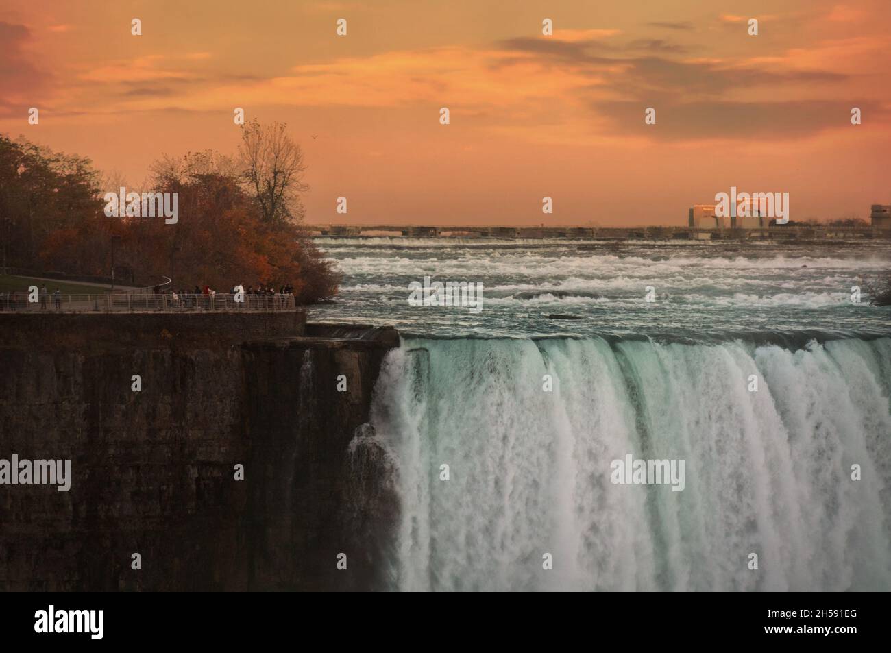 Green waters of Niagara river dashing downd from the edge of Horseshoe Falls in front of spectacular sunset sky. Horseshoe Falls, also known as Canadi Stock Photo