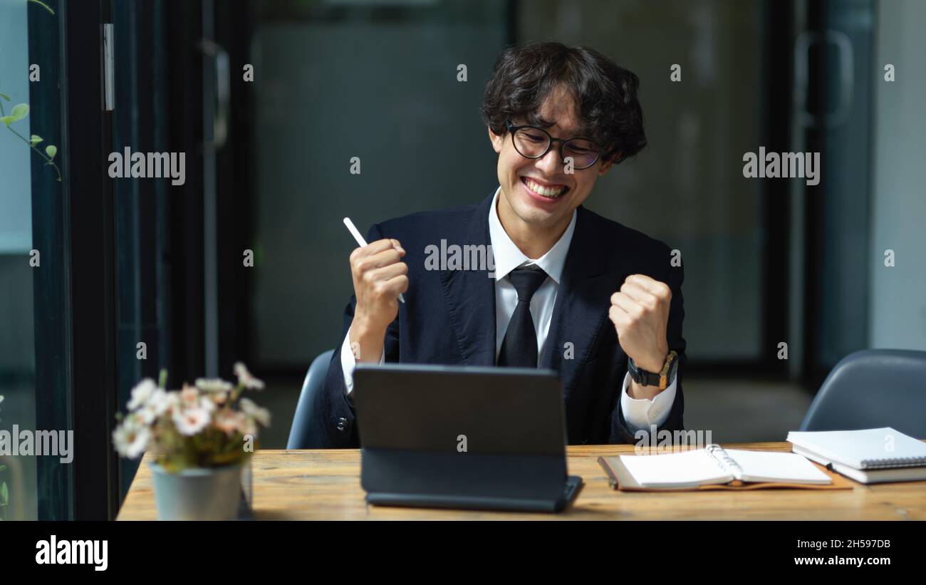 Asian young businessman extremely happy and satisfied on his project. Excited male executive at his desk. Work promotion. Stock Photo